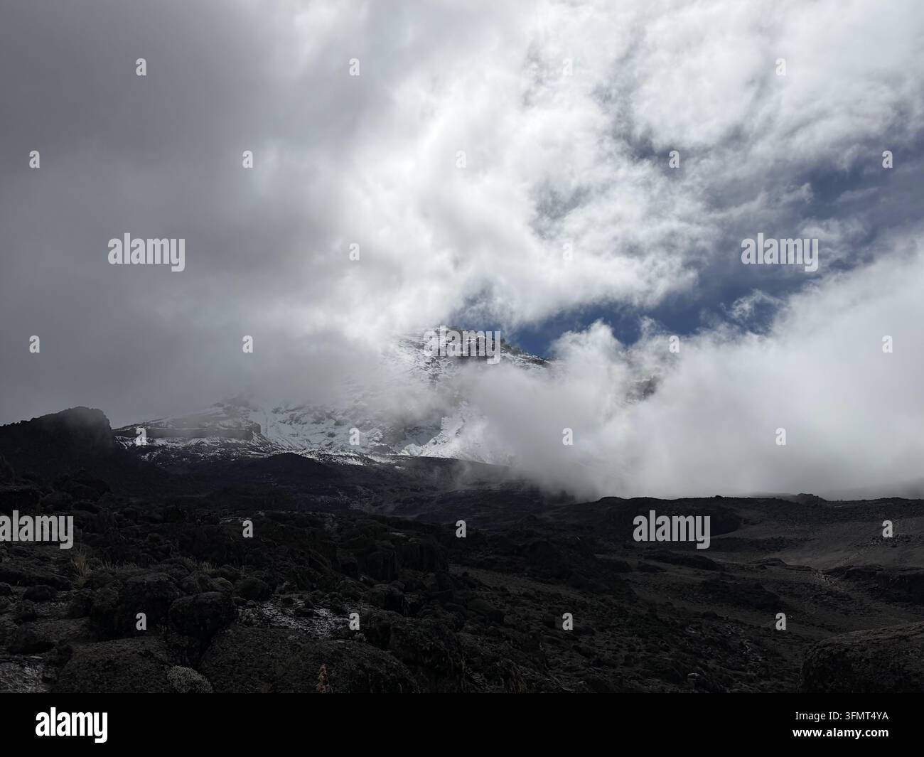 I pendii superiori bianchi del Kibo emergono tra le nuvole sopra un terreno vulcanico nero sul Monte Kilimangiaro, Tanzania. - Immagine stock catturata con smartphone