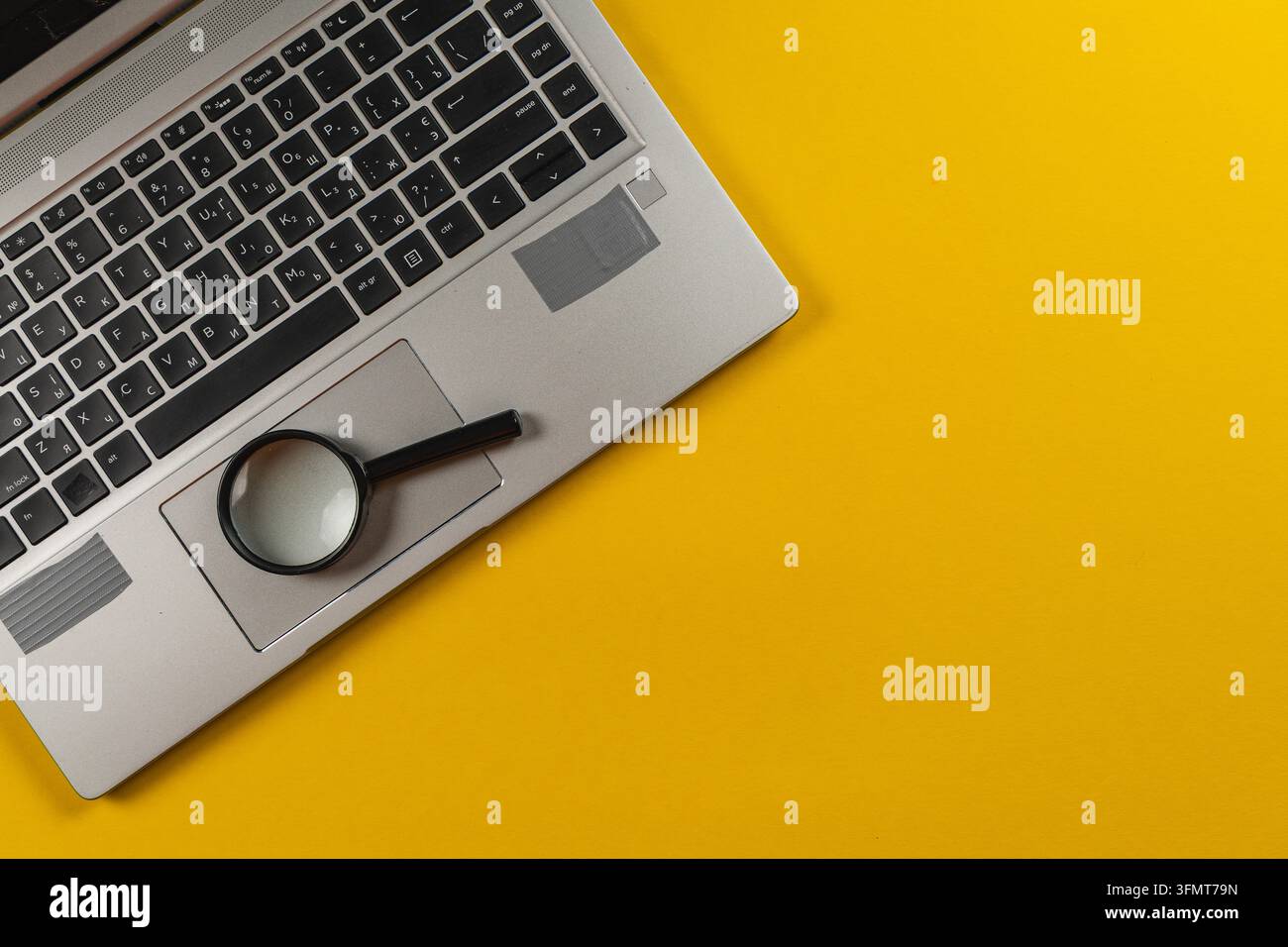 Una lente d'ingrandimento poggia su un laptop mentre la ricerca avviene su uno sfondo giallo, concentrandosi sui dettagli e l'analisi. Foto Stock