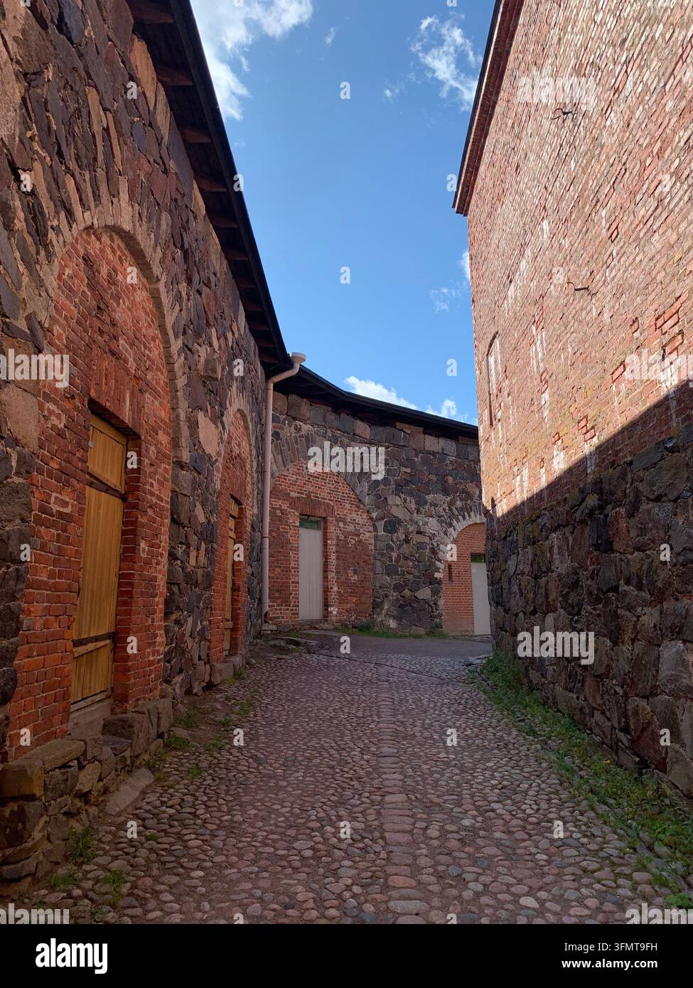 Sentiero di ciottoli fiancheggiato da edifici storici in pietra e mattoni a Helsinki, Finlandia. Le strutture presentano portali ad arco con porte in legno e metallo Foto Stock