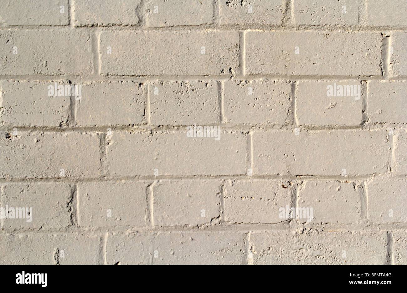 Primo piano della trama di un muro di mattoni dipinto con file di mattoni color crema, giunti di malta irregolari e una superficie leggermente consumata Foto Stock