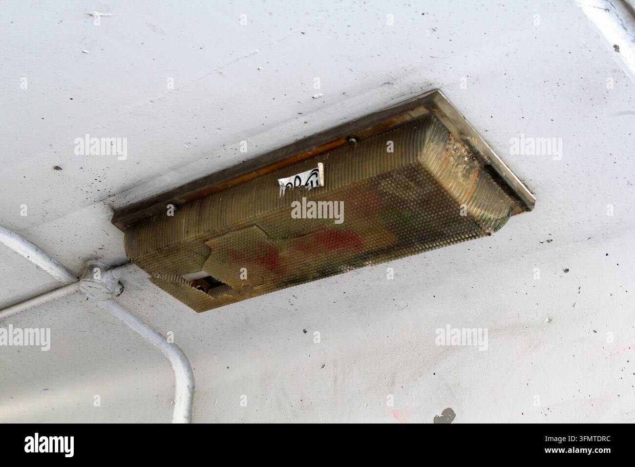 Apparecchio di illuminazione fluorescente rettangolare coperto di sporco e patina montato su un soffitto bianco macchiato Foto Stock