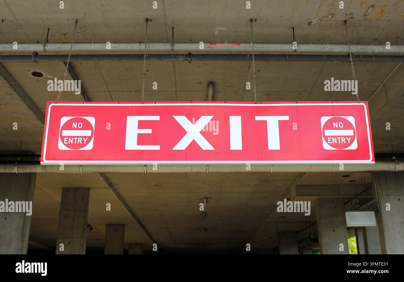 Un cartello di uscita rosso sospeso con lettere bianche e simboli "No Entry" in un parcheggio di cemento Foto Stock