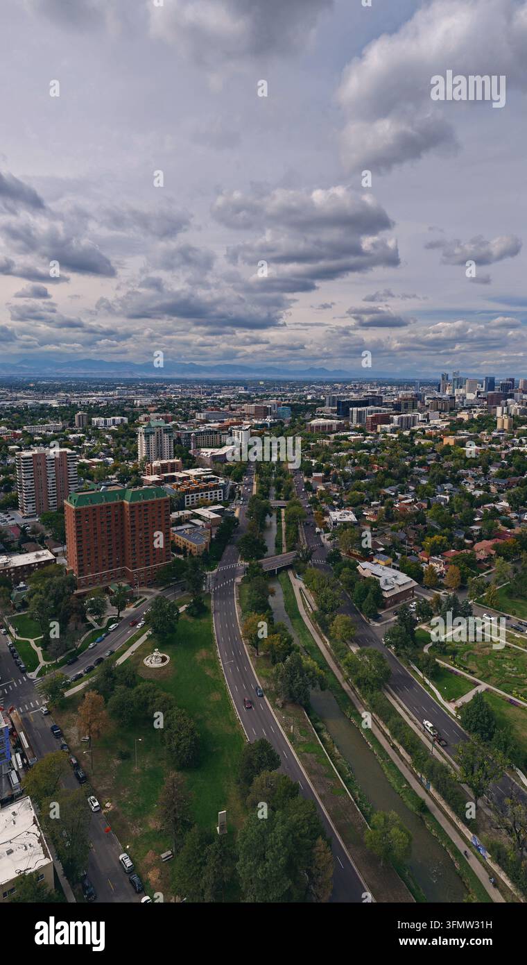Vista aerea di Cherry Creek che si snoda attraverso il paesaggio urbano con alberi rigogliosi, strade cittadine e lo skyline di Denver sotto un cielo nuvoloso a Denver, Co Foto Stock