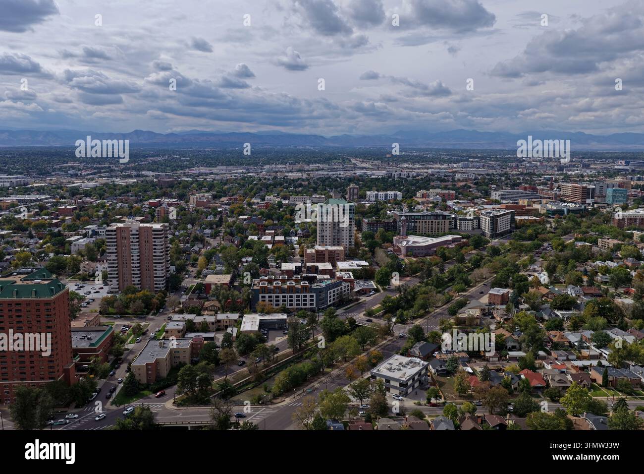 Vista aerea del quartiere Cherry Creek con edifici alti, alberi rigogliosi e infrastrutture urbane sotto un cielo nuvoloso con montagne lontane Foto Stock