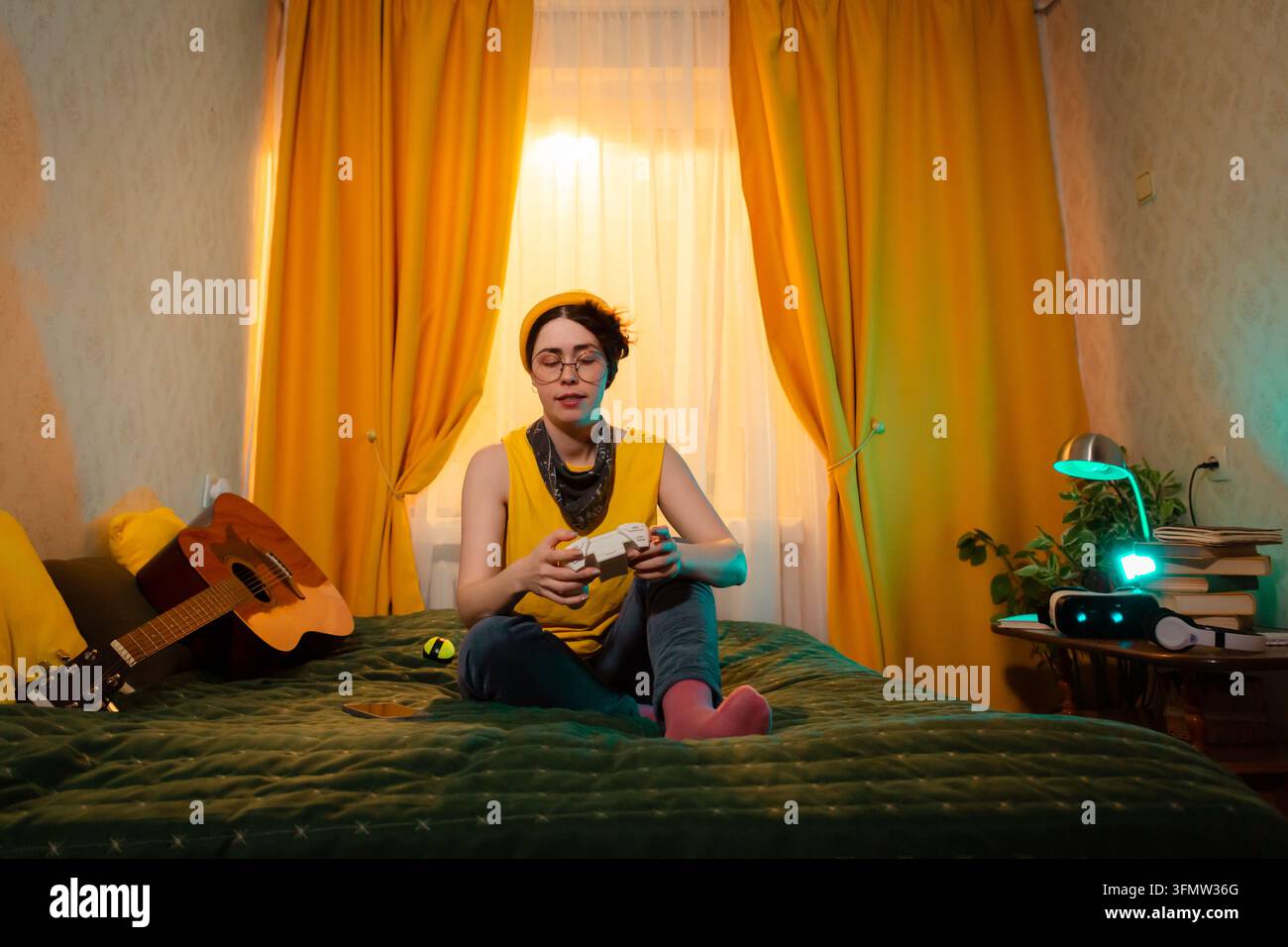 Adolescente seduto sul letto e gioca ai videogiochi mentre è immerso nella calda luce del tramonto. Concetto di equilibrio emotivo e tempo sullo schermo. Inquadratura ampia, vista dall'alto. Foto Stock