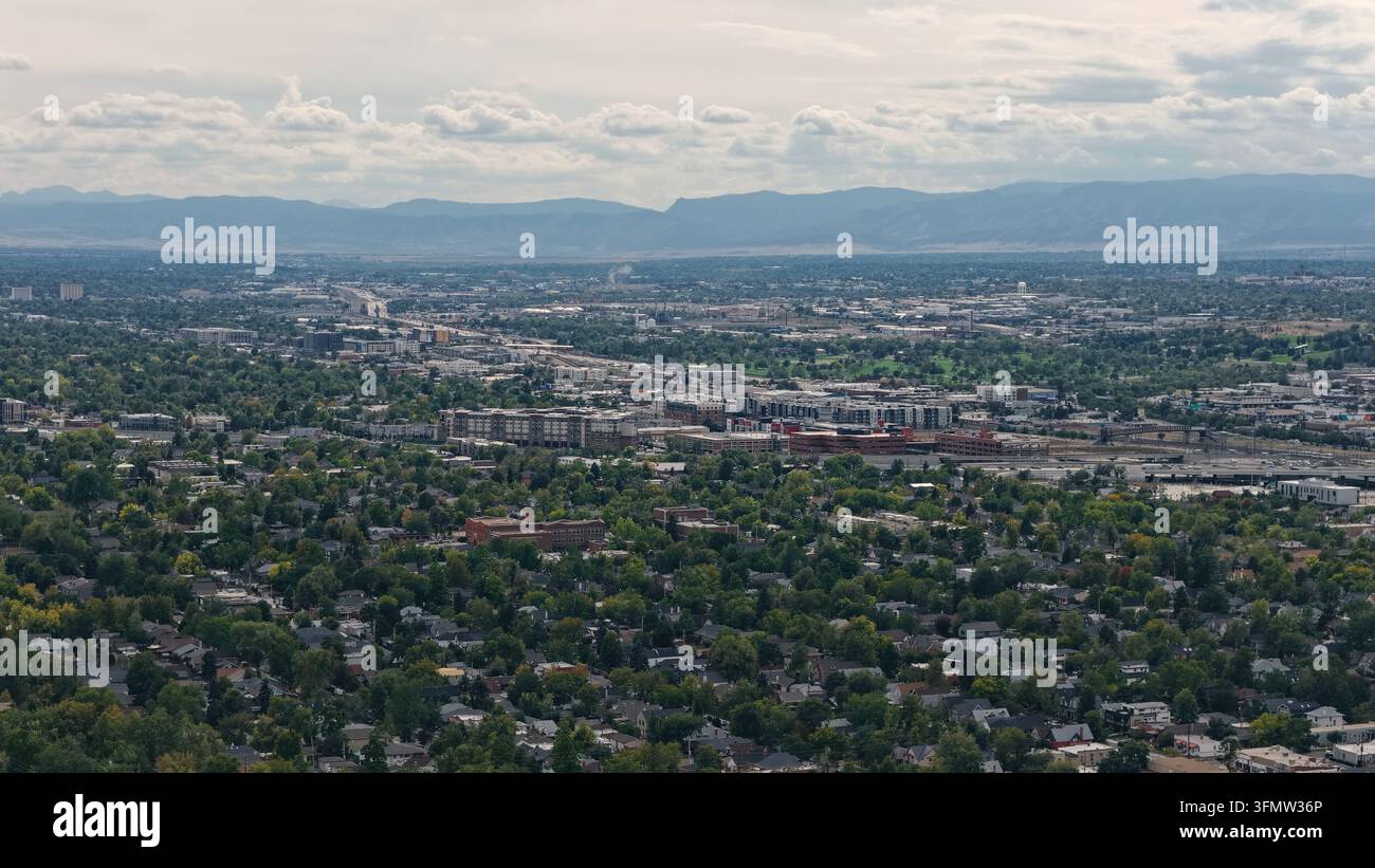 Veduta aerea dell'area di Cherry Creek con alberi verdi lussureggianti, quartieri residenziali e infrastrutture urbane sotto un cielo nuvoloso con montagne in lontananza Foto Stock