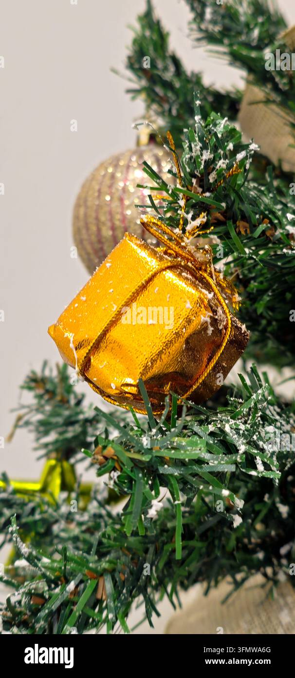 Decorazione natalizia in scatola regalo dorata appesa tra i rami degli alberi verdi ricoperti di neve con una sfera pallida sullo sfondo, Granada, Spagna. Foto Stock