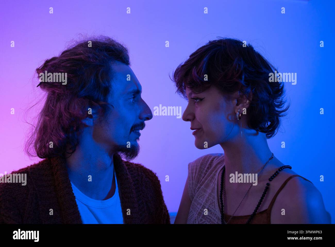Coppia che scambia uno sguardo intenso alla luce al neon durante un momento di appuntamento, esprimendo attrazione, chimica, romanticismo, intimità, fiducia e tensione emotiva. Foto Stock