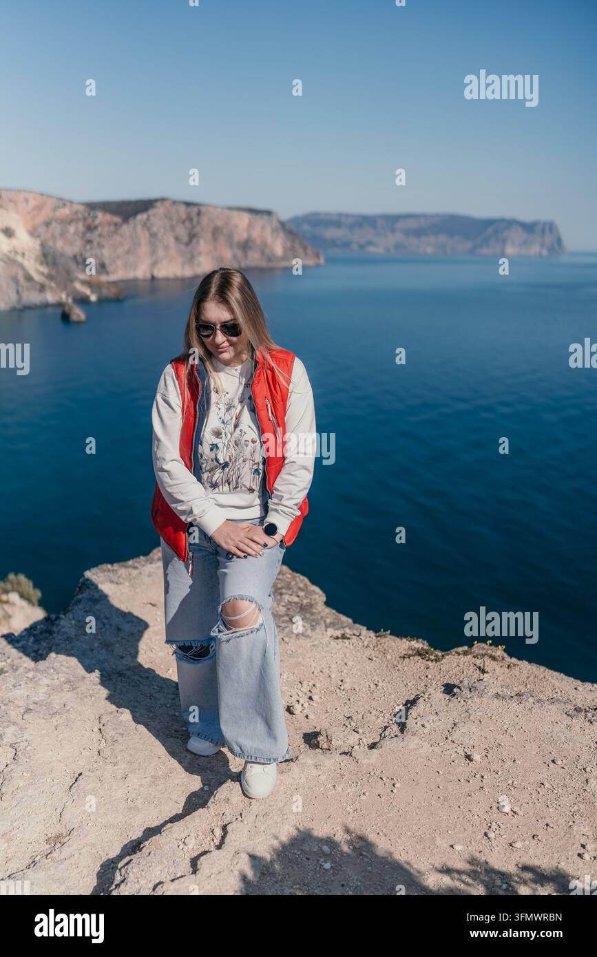 Donna in piedi su un dirupo roccioso sul mare che gode del paesaggio costiero scenografico sotto un cielo blu terso Foto Stock