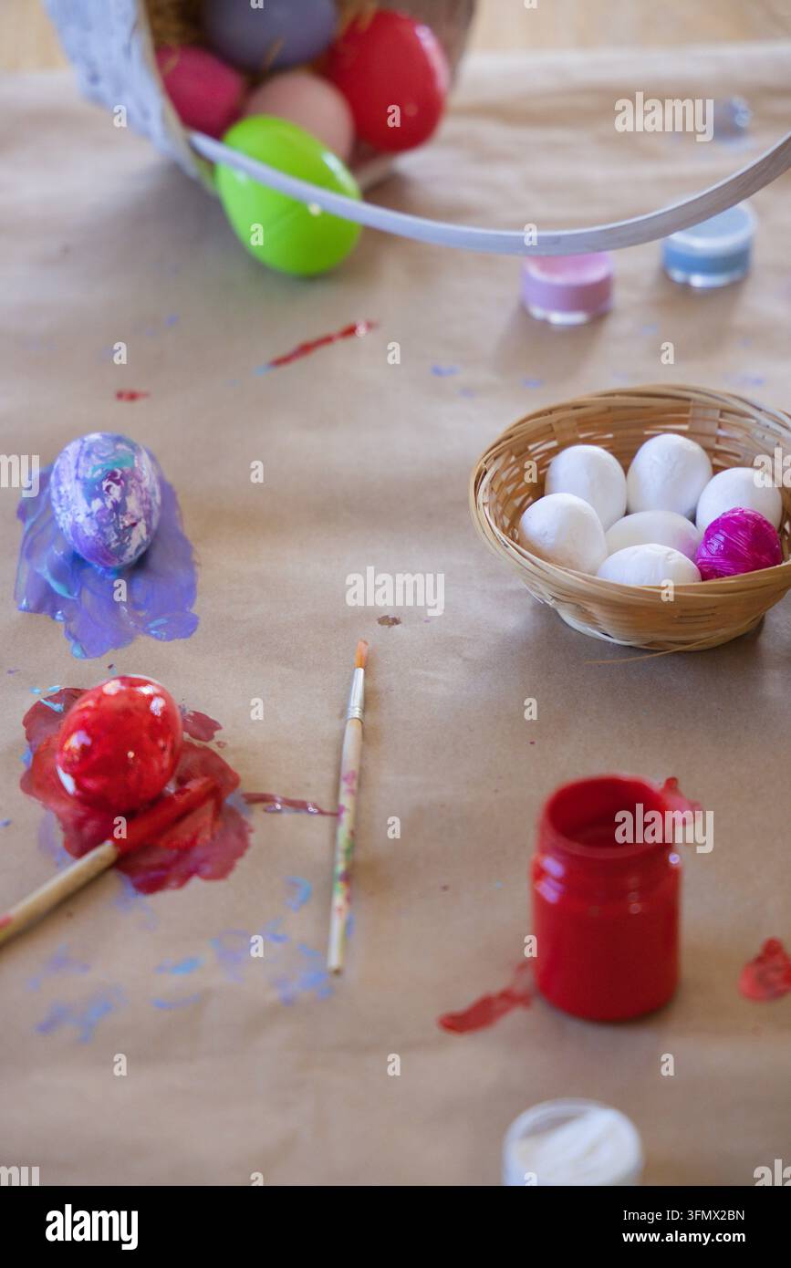 Cesto intrecciato contiene sette uova su carta kraft con uova dipinte e pennello nelle vicinanze Foto Stock