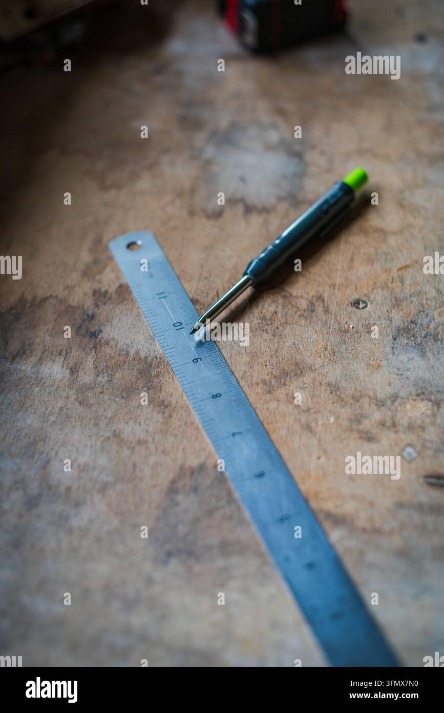 Vista di un righello di metallo e di una matita meccanica appoggiati su un banco di lavoro in legno consumato a Looe, Cornovaglia, Regno Unito. Foto Stock
