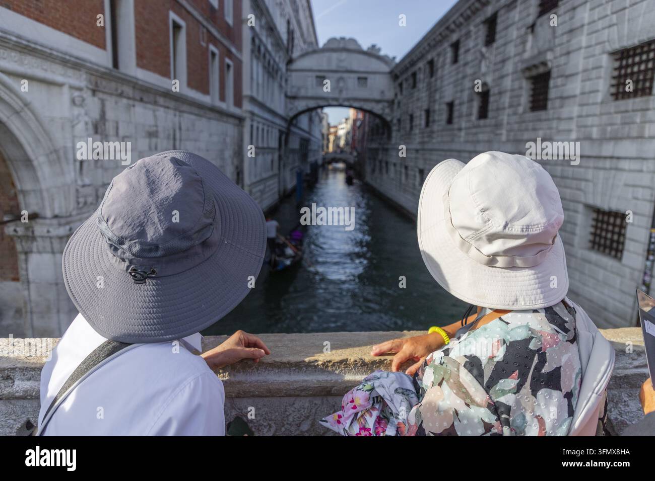 Vista di due persone con cappelli da sole che osservano il ponte dei Sospiri storico su un canale a Venezia, Veneto, Italia. Foto Stock