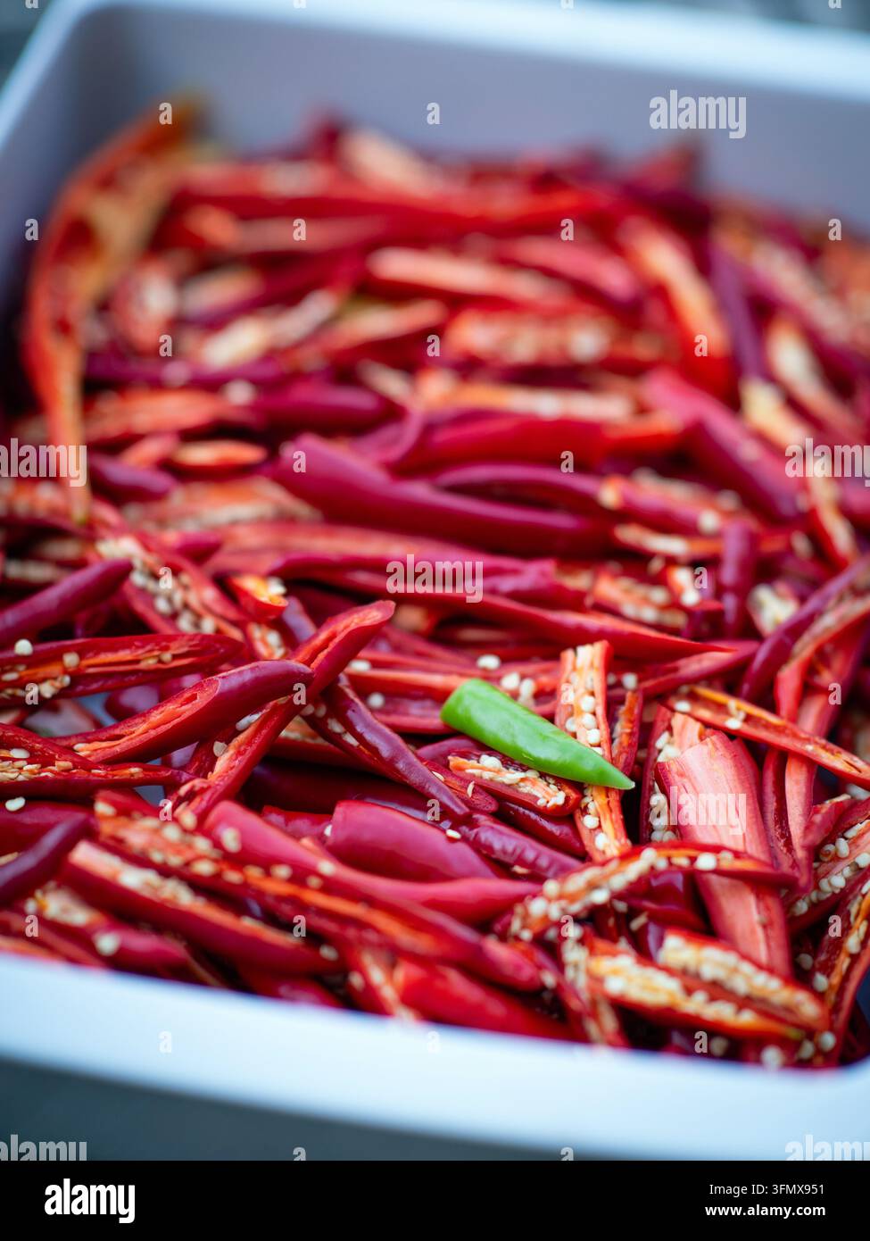 Un peperoncino verde tra peperoncini rossi affettati in un vassoio bianco Foto Stock