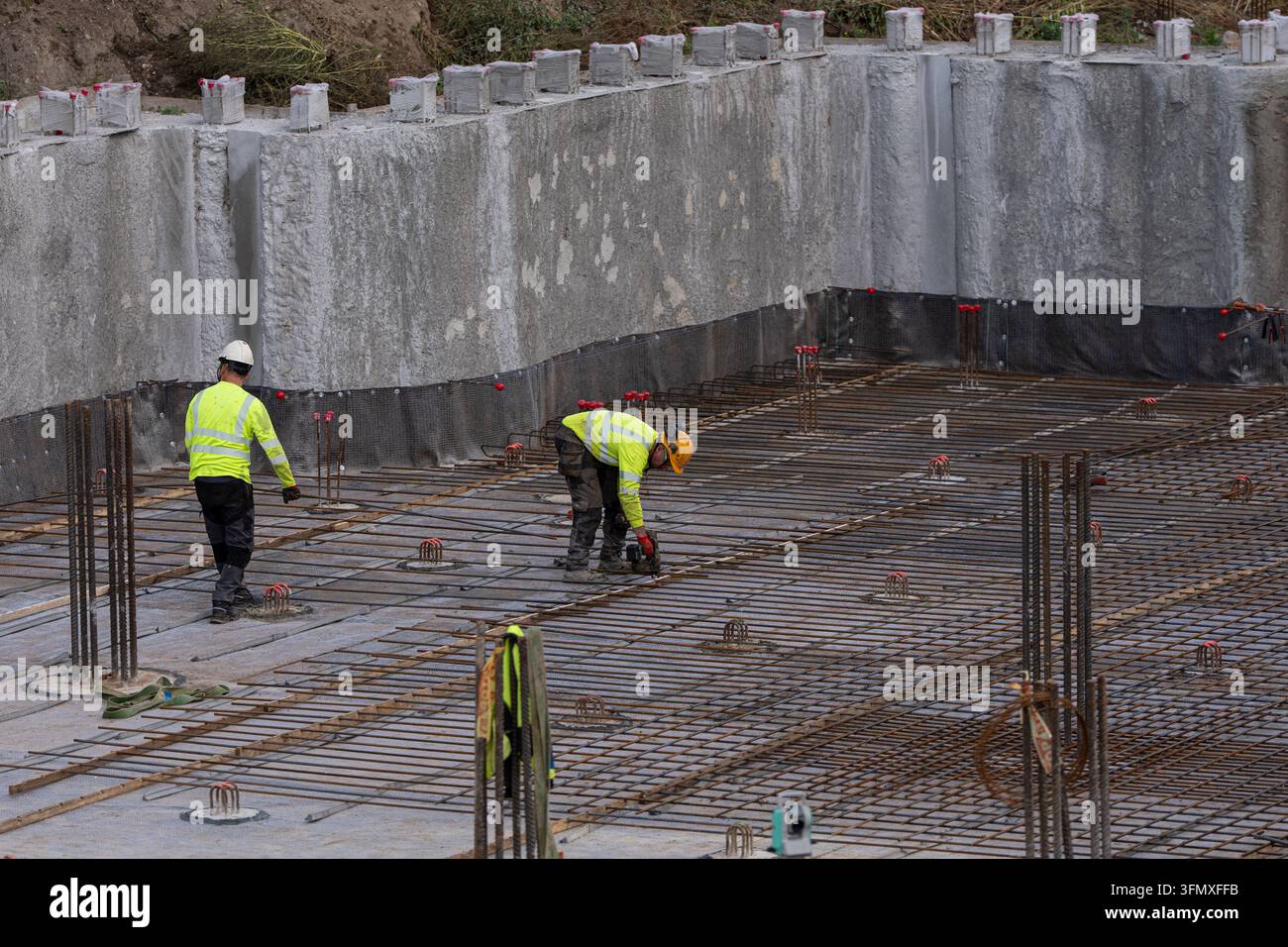 Operai edili che installano rinforzi in acciaio all'interno di pareti di fondazione in cemento, concetto di cantiere per infrastrutture Foto Stock