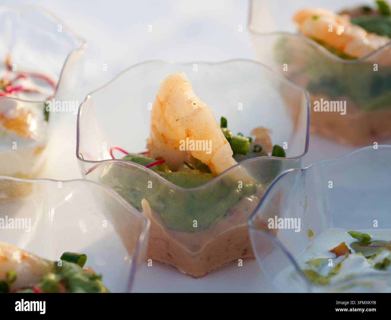 Piccole porzioni di antipasti di cocktail di gamberetti con salsa ed erbe in coppette di plastica trasparenti. Foto Stock