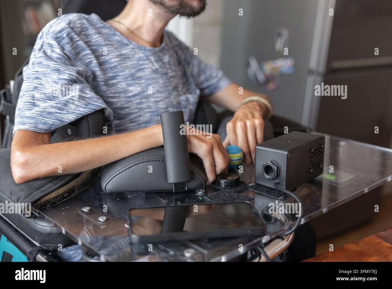 Un uomo utilizza una tecnologia di assistenza per controllare la sua sedia a rotelle nella sua zona giorno. Interagisce con l'attrezzatura per una vita indipendente. Foto Stock
