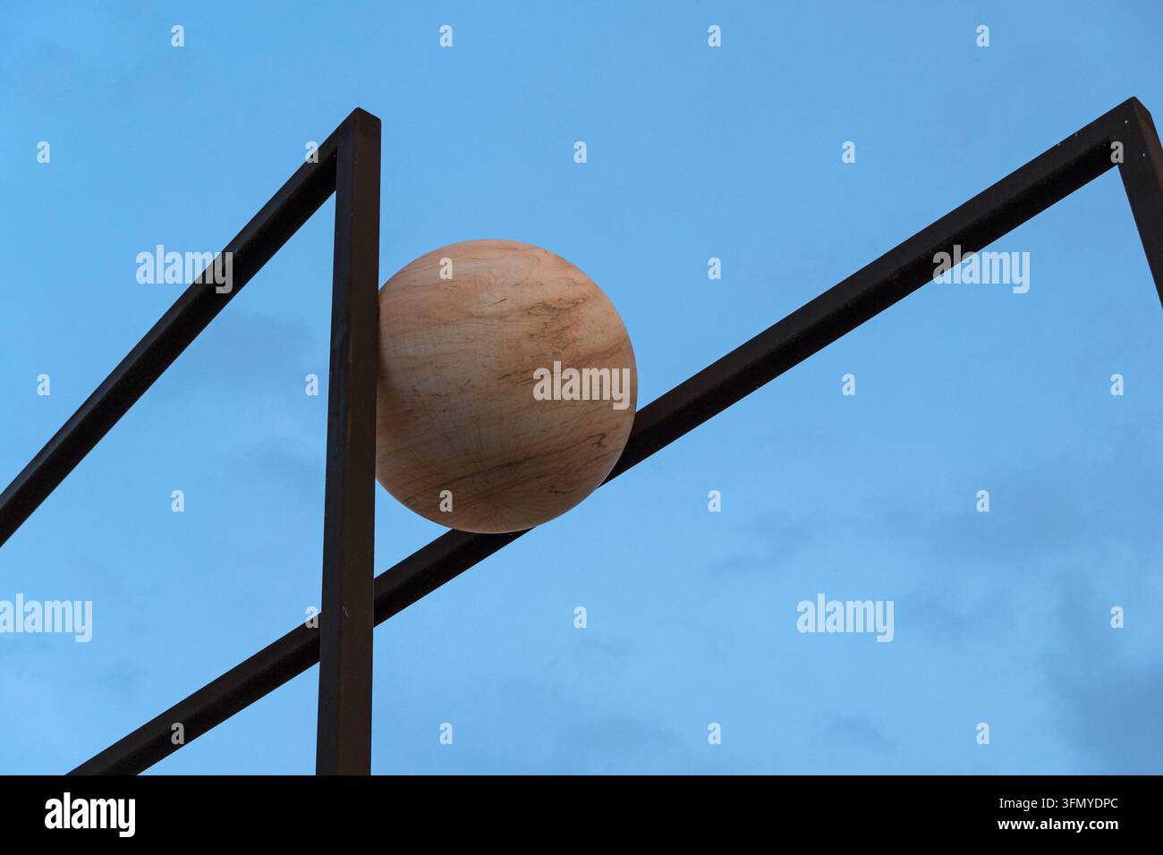 Un'installazione artistica all'aperto minimalista con una sfera di pietra bilanciata tra telai metallici contro un cielo blu serale dell'artista Alicja Kwade Foto Stock