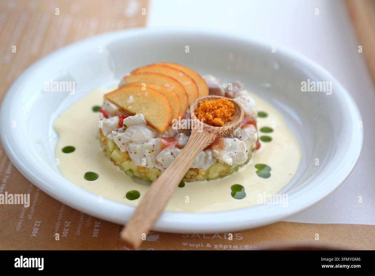 Antipasto di frutti di mare gourmet servito con pesche affettate, salsa cremosa, olio alle erbe e condimento croccante in una ciotola bianca, presentato con un piatto elegante. Foto Stock