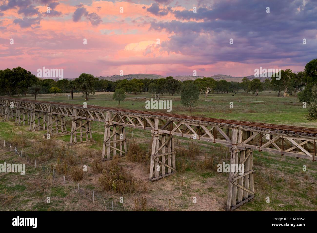 Storico ponte a traliccio ferroviario in legno attraversa la campagna aperta vicino a Gundagai, New South Wales, Australia, sotto un drammatico tramonto rosa e viola s Foto Stock