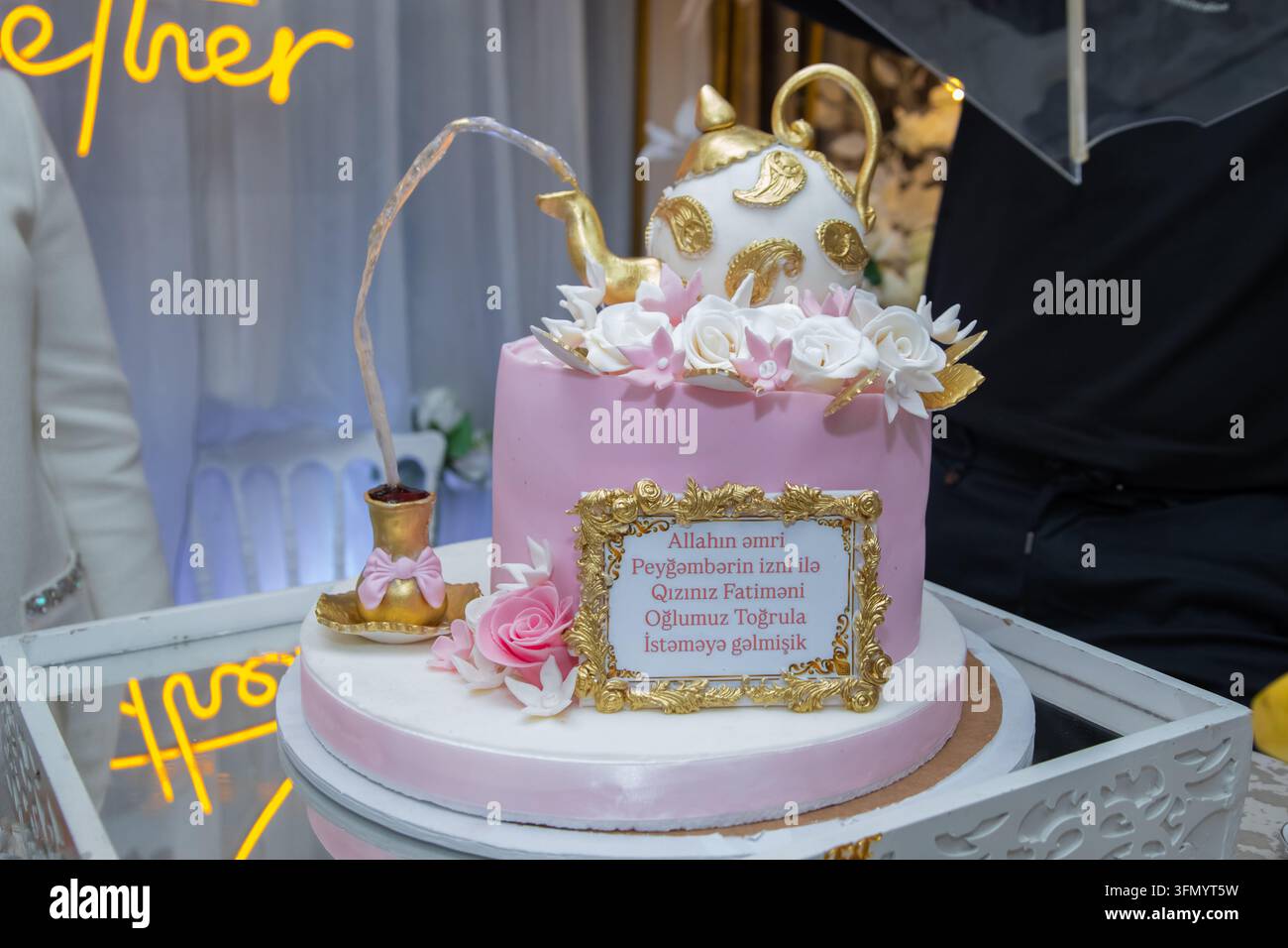 Decorazione lussuosa per torta da festa con accenti dorati in un luogo speciale per celebrazioni. Elegante torta di compleanno bianca a più piani su supporto davanti a una foto Foto Stock