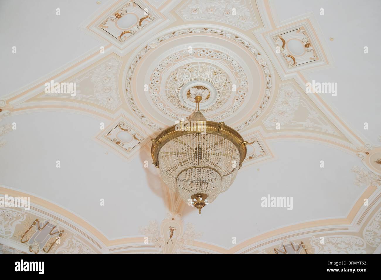 Apparecchio di illuminazione interno di lusso con ornamento in gesso dettagliato sul soffitto bianco.Vista dal basso di un grande lampadario in cristallo vintage appeso da Foto Stock