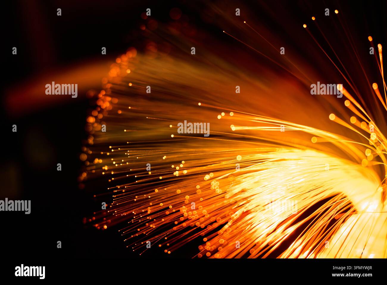 Primo piano di filamenti di fibra ottica arancioni luminosi che si irradiano su uno sfondo scuro, creando una visione astratta del trasferimento di dati ad alta velocità, comunicazione Foto Stock
