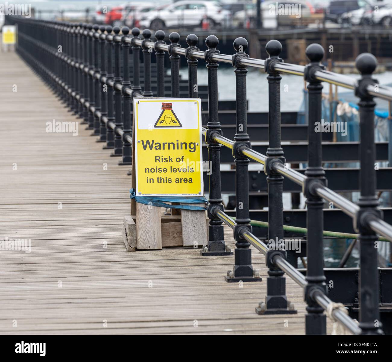 Segnale di avvertimento sui livelli sonori elevati accanto alle ringhiere nere su una passerella in legno sul lungomare di Ryde Isle of Wight Foto Stock
