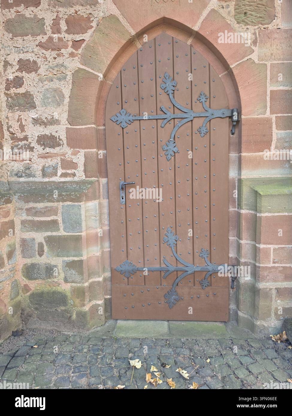 Antica porta ad arco in legno storica con cerniere decorative in ferro battuto inserite in un muro di pietra medievale - Immagine stock catturata con smartphone