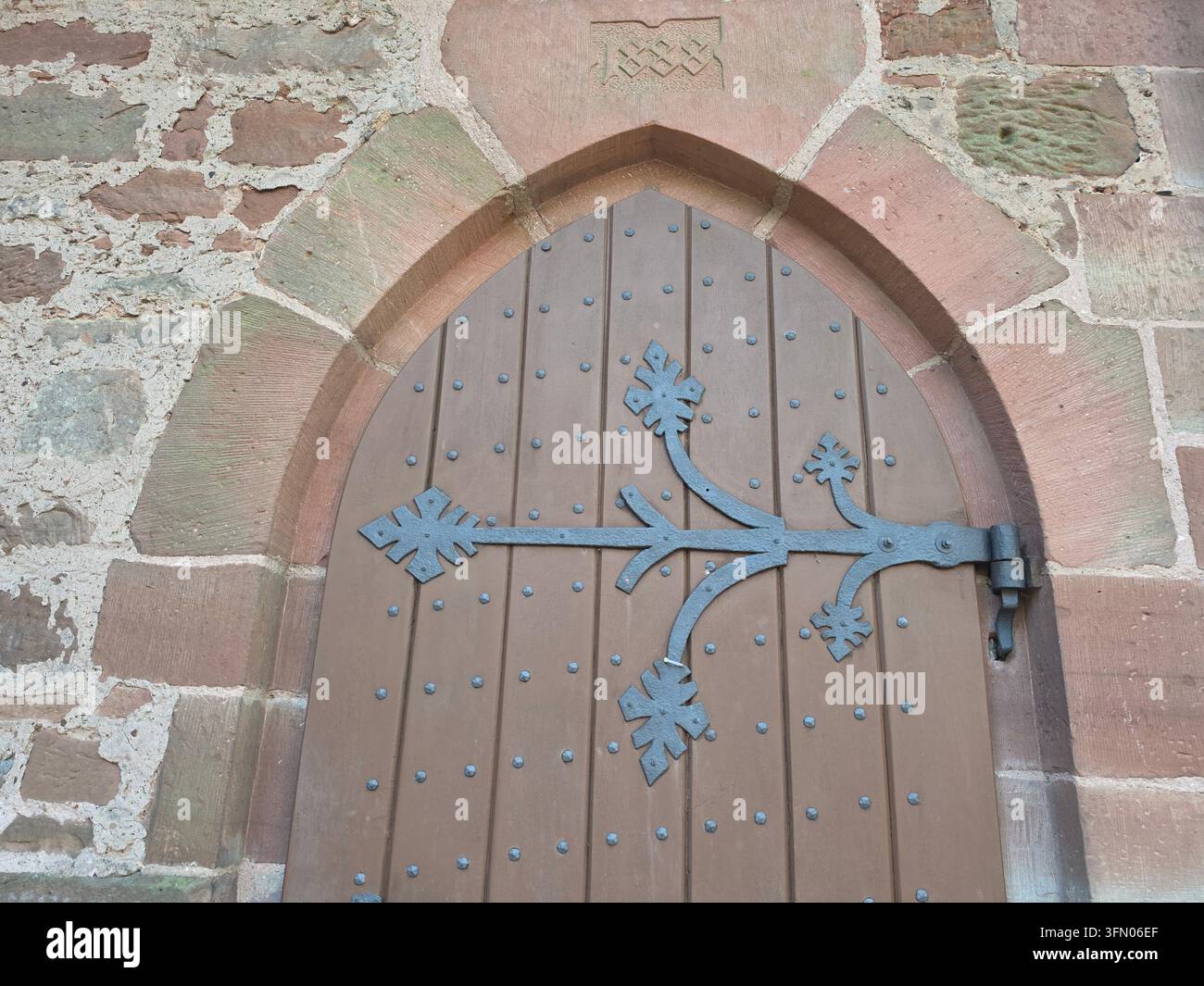 Primo piano di una porta ad arco in legno antica storica con cardini in ferro battuto in un muro di pietra - Immagine stock catturata con smartphone