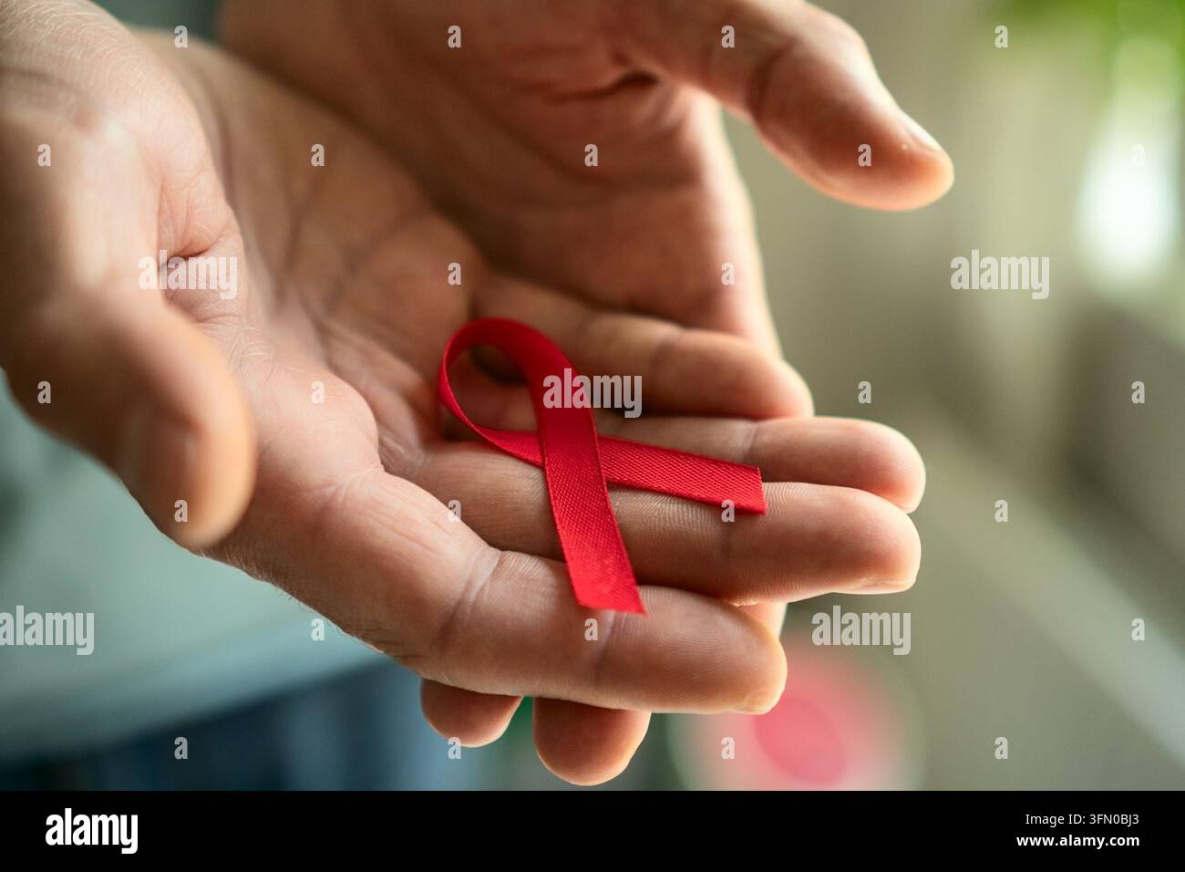 Mani maschili che tengono con cura il nastro rosso di sensibilizzazione, che rappresenta la solidarietà con le persone sieropositive e il mese di sensibilizzazione di dicembre. Foto Stock