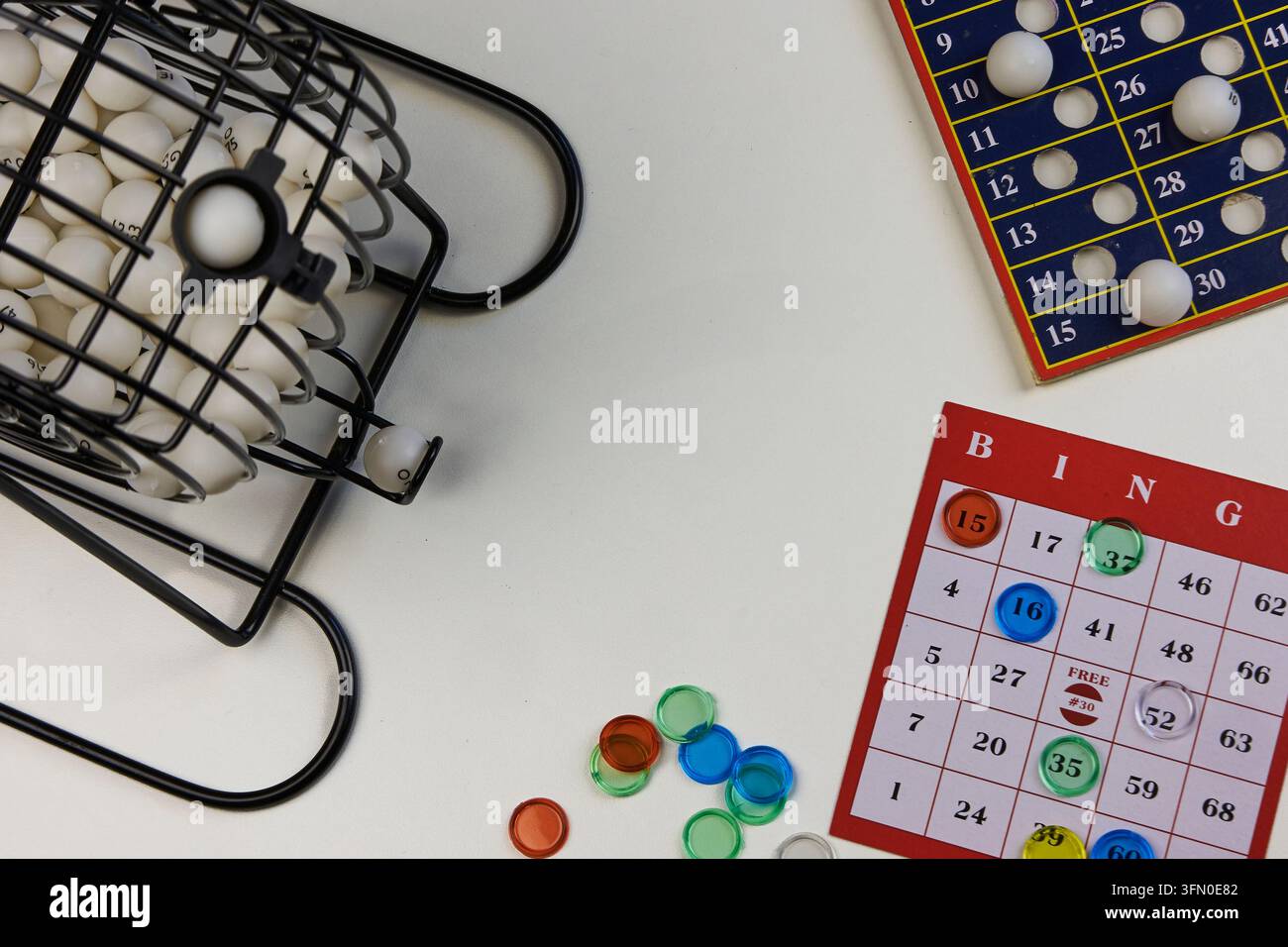 Configurazione del gioco del bingo su una superficie bianca, che mostra una gabbia, palline, carte e pennarelli colorati Foto Stock
