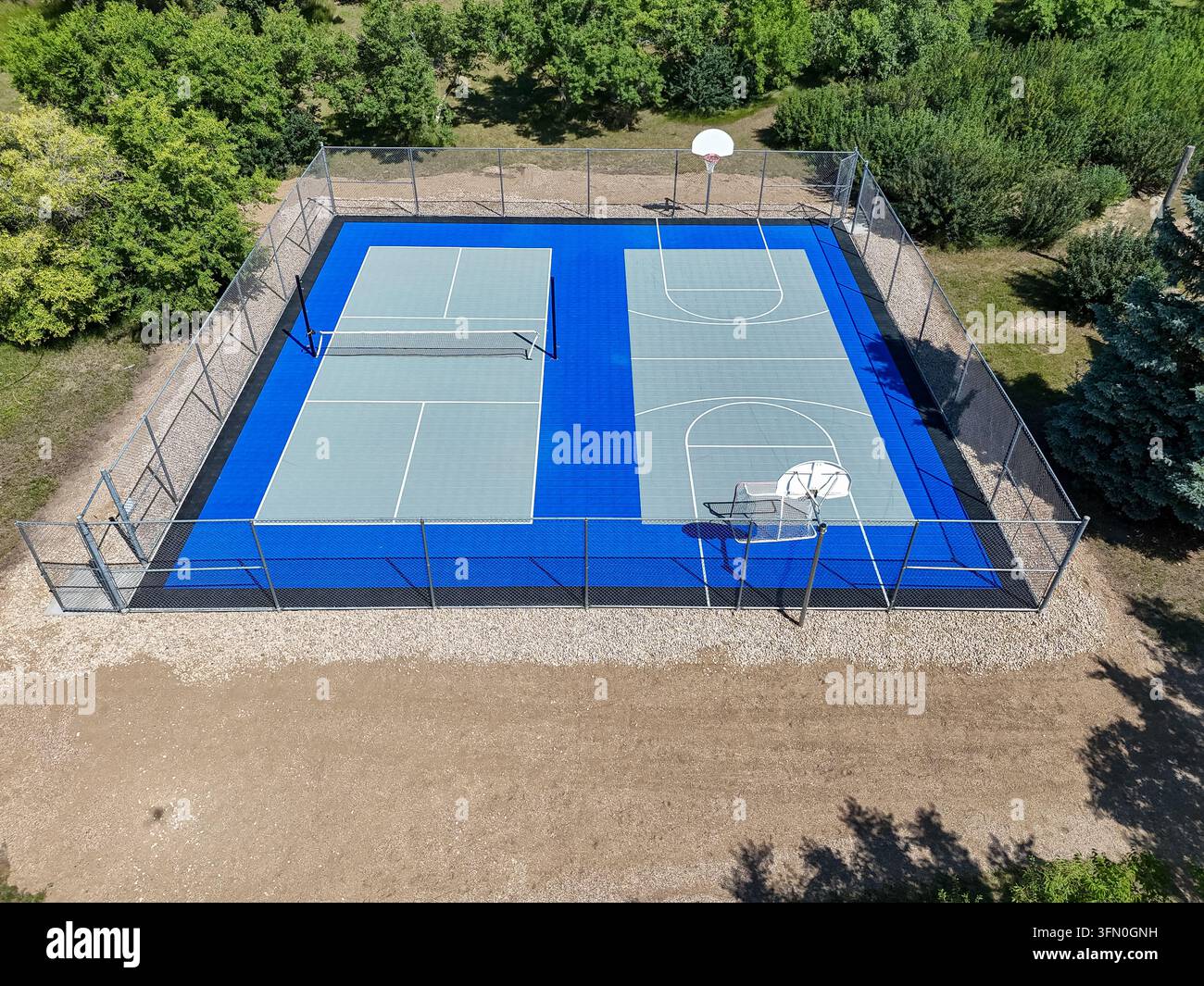 Vista aerea mostra un campo multisport circondato dalla vegetazione. La superficie blu e grigia presenta zone per il basket e il tennis. Una recinzione delimita l'area per la sicurezza Foto Stock