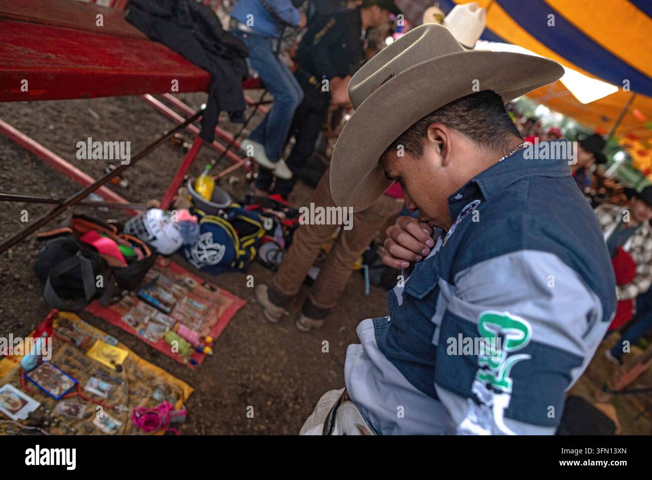 Città del Messico, Messico. 29 settembre 2026. Un cavaliere di jaripeo in camicia grigia e ampio cappello da cowboy china la testa con una mano vicina al petto accanto a un'immagine devozionale a terra, a San Miguel Topilejo, Città del Messico, Messico, il 29 settembre 2026. Prima dell'evento, i cavalieri posizionavano immagini di santi e altri oggetti devozionali su teli, tracciavano il segno della croce e partecipavano alla tradizionale preghiera del cavaliere cercando protezione prima di entrare nell'arena. (Foto di Xavier Duarte/Middle East Images/StringersHub/Sipa USA) Credit: Sipa USA/Alamy Live News Foto Stock