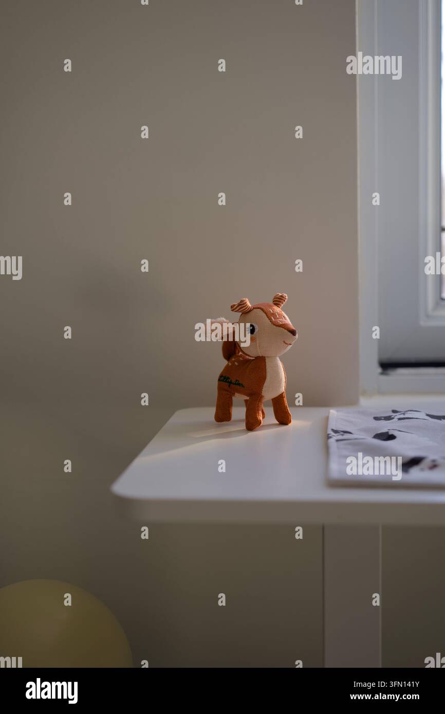 Simpatico peluche di cervo su tavolo bianco vicino alla finestra alla luce calda del sole Foto Stock