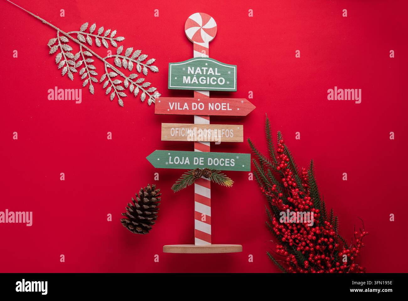 Segnale direzionale natalizio festivo con varie destinazioni festive su uno sfondo rosso vivace. Include coni di pino, accenti di fiocco di neve, glitter argento Foto Stock