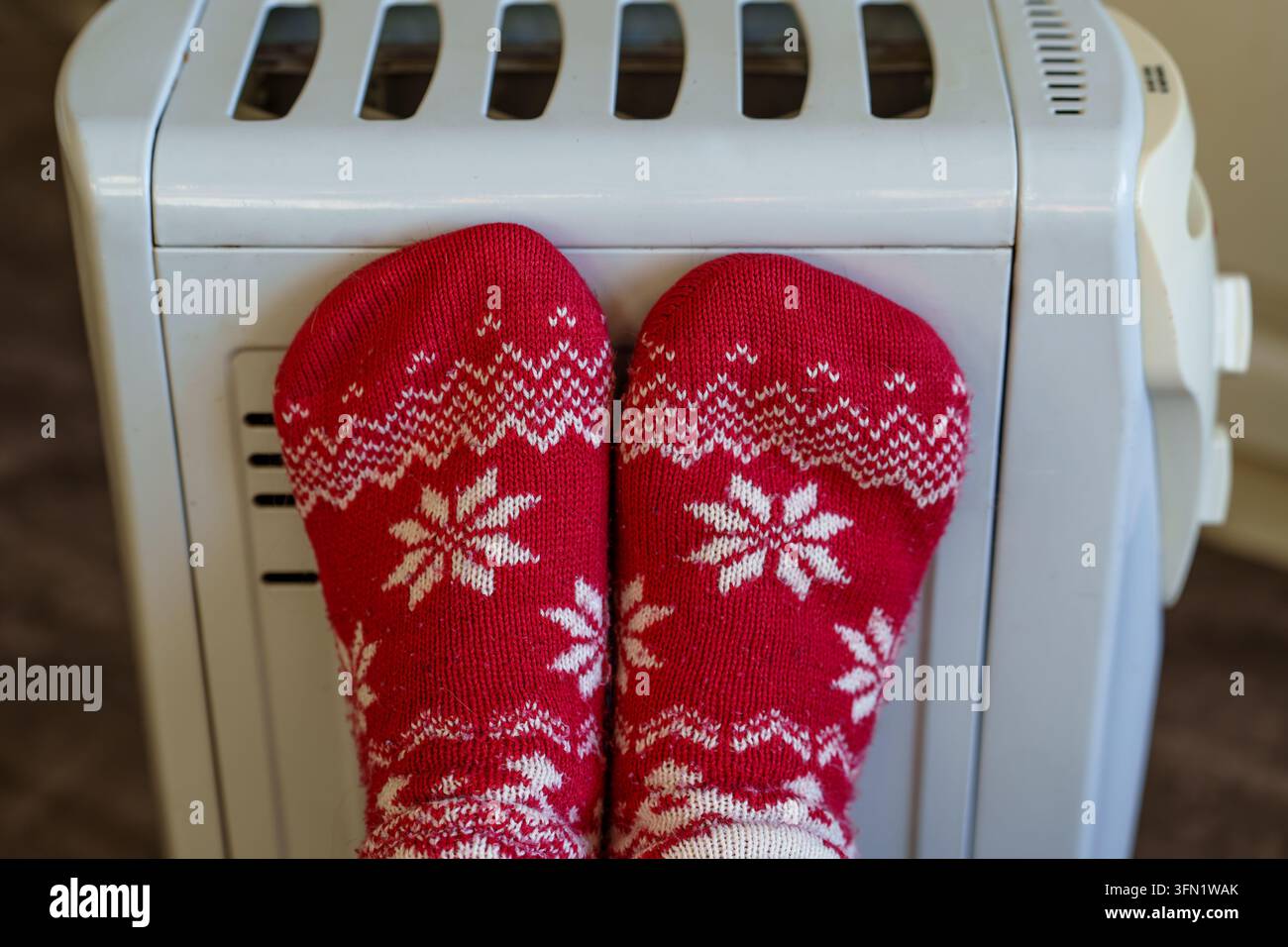 Piedi calzati nel calzino che si riscaldano vicino a un termostufa elettrica. Il concetto di preparazione invernale e comfort stagionale domestico Foto Stock