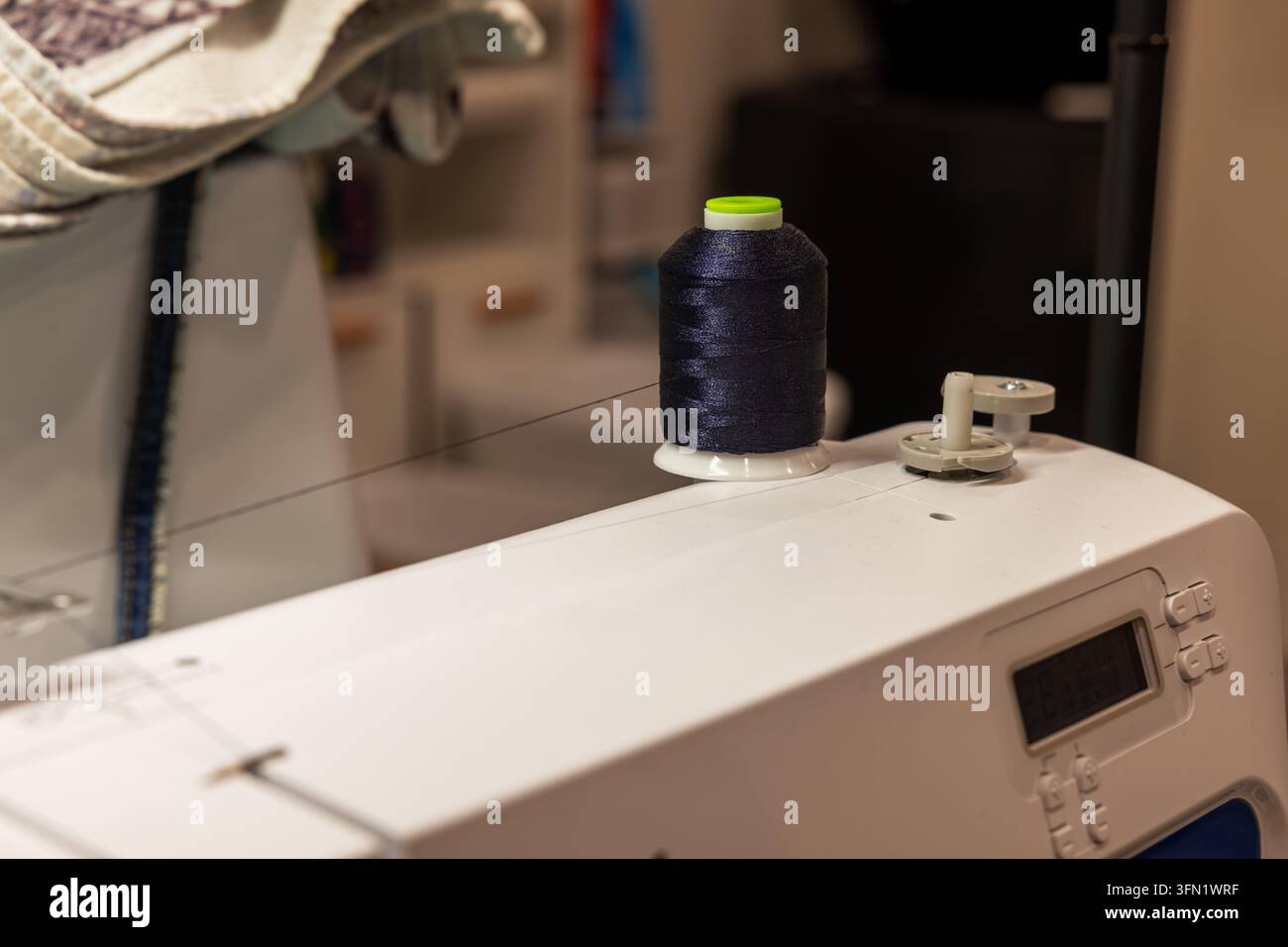 Prima di una macchina da cucire con bobina di filo scuro, filo, tessuto e tappetino da taglio sullo sfondo Foto Stock