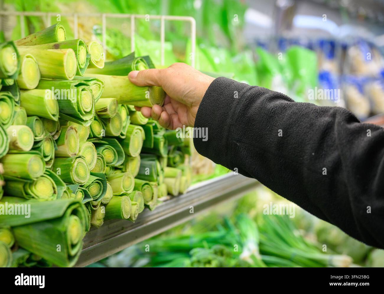 Mano di un uomo che raccoglie porro fresco dallo scaffale di un negozio di alimentari. California. USA. Foto Stock