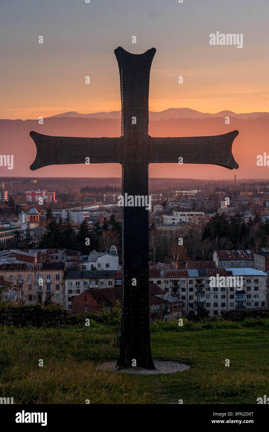 Vista verticale di una croce cristiana che si affaccia su Kutaisi, Georgia, con il paesaggio urbano storico e le colline verdi dell'Imereti che si estendono in lontananza. Foto Stock