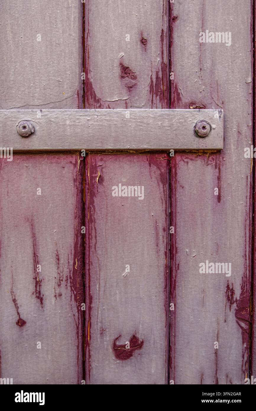 Antica porta di legno viola con vernice scrostata, superficie consumata, dettaglio serratura in metallo, viti, sfondo texture vintage rustico Foto Stock