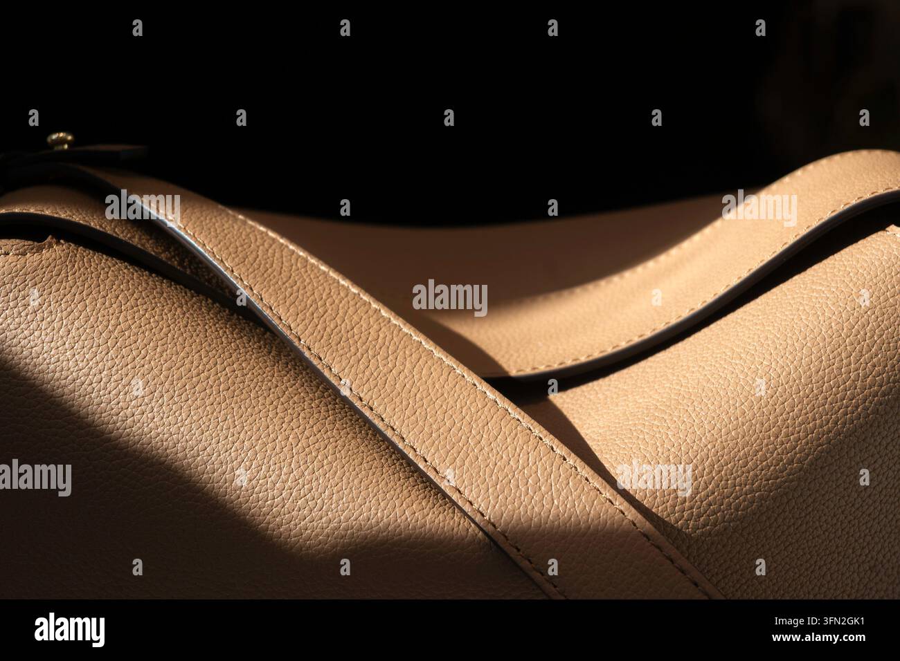 Borsa da donna in pelle marrone chiaro alla moda in macchia di sole su sfondo scuro Foto Stock
