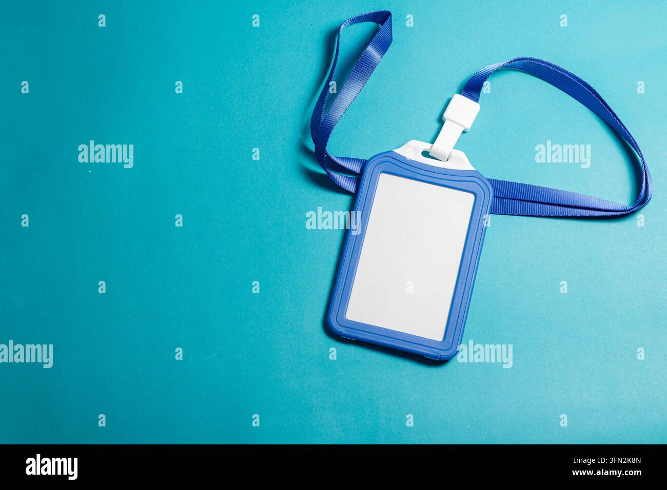 Un portabadge di plastica blu vuoto con un cordino a nastro posizionato su uno sfondo blu ciano vivace, ideale per conferenze aziendali o mockup d'ufficio. Foto di alta qualità Foto Stock