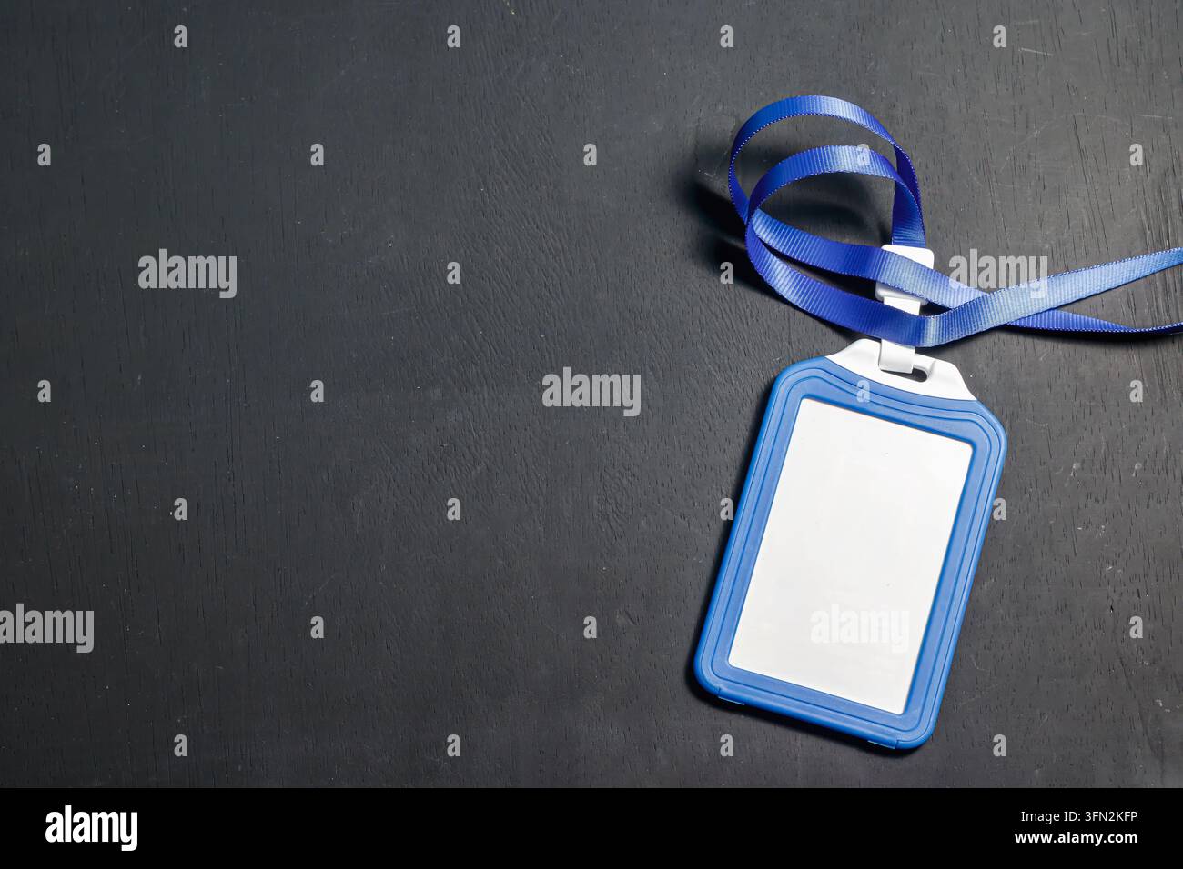 Un portabadge in plastica blu vuoto con un cordino a nastro appoggiato su uno sfondo scuro testurizzato, ideale per conferenze aziendali o mockup aziendali. Foto di alta qualità Foto Stock