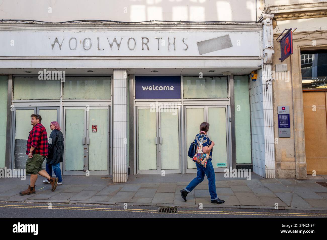 Le persone camminano sul marciapiede davanti a un edificio commerciale chiuso di Woolworths con un cartello vintage sbiadito e porte d'ingresso in vetro sbarrate. Foto Stock
