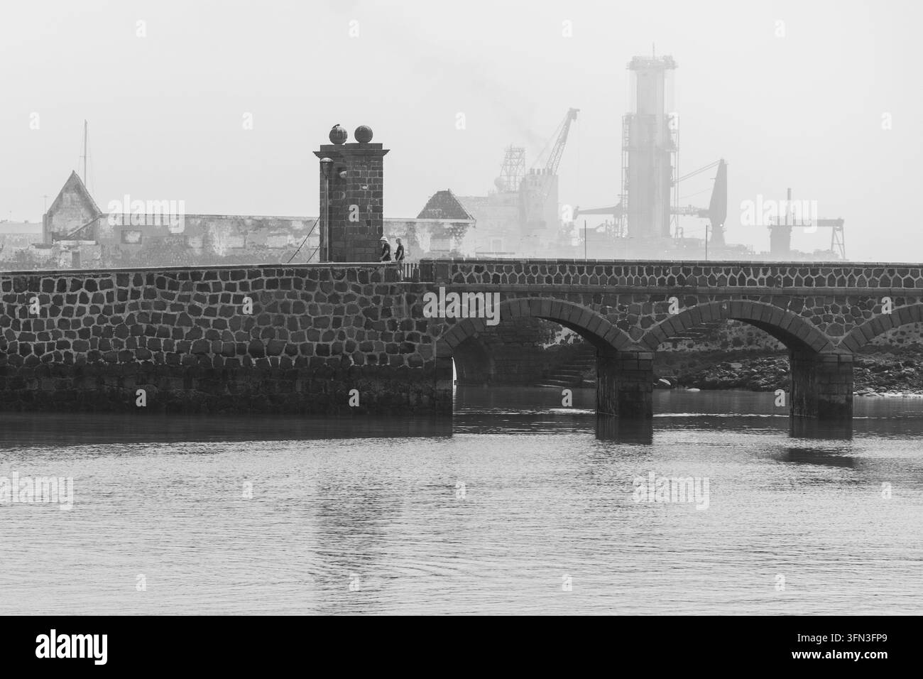 Storico Puente de las Bolas ad Arrecife visto nella nebbia, con le gru moderne del porto che svaniscono sullo sfondo. Foto Stock