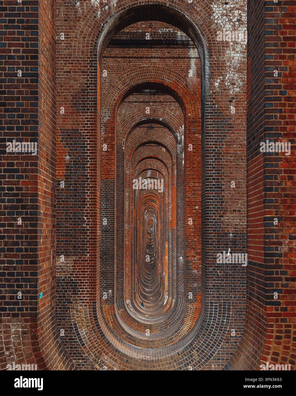 Archi ripetuti in mattoni rossi visti attraverso i pilastri traforati del viadotto della valle dell'Ouse, Balcombe, West Sussex, Regno Unito Foto Stock