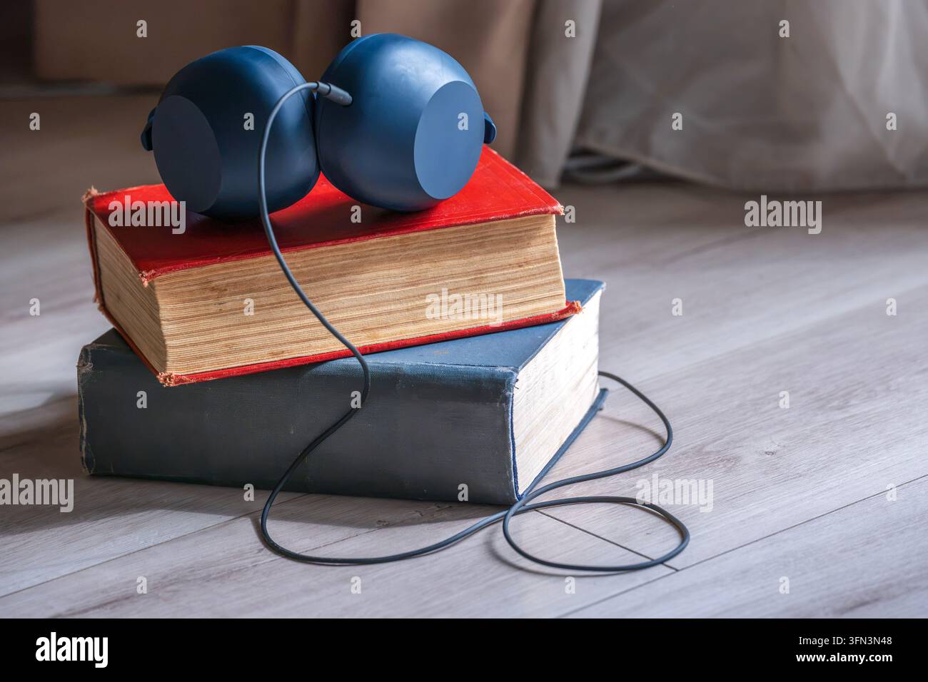 Auricolari posizionati su libri vintage impilati, simboleggiando la fusione della lettura tradizionale con i contenuti audio digitali e l'apprendimento Foto Stock