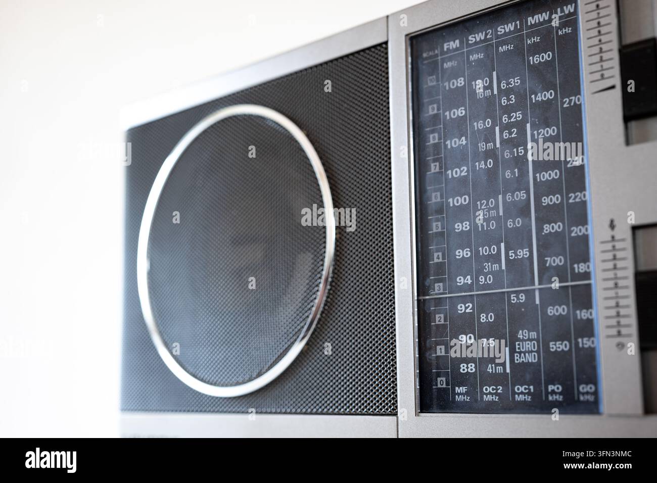 Vista dettagliata di una radio portatile classica in argento con una griglia del altoparlante frontale e una scala analogica di visualizzazione della frequenza radio in luce interna soffusa Foto Stock