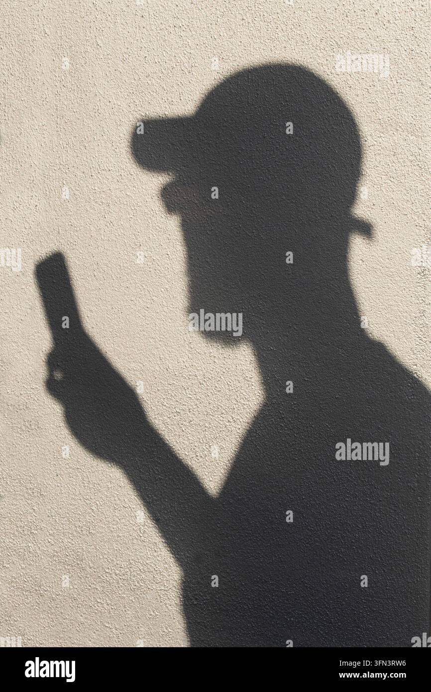 Silhouette anonima di una persona che usa uno smartphone, evocando privacy, anonimato, comunicazione digitale e il lato nascosto della tecnologia. Foto Stock
