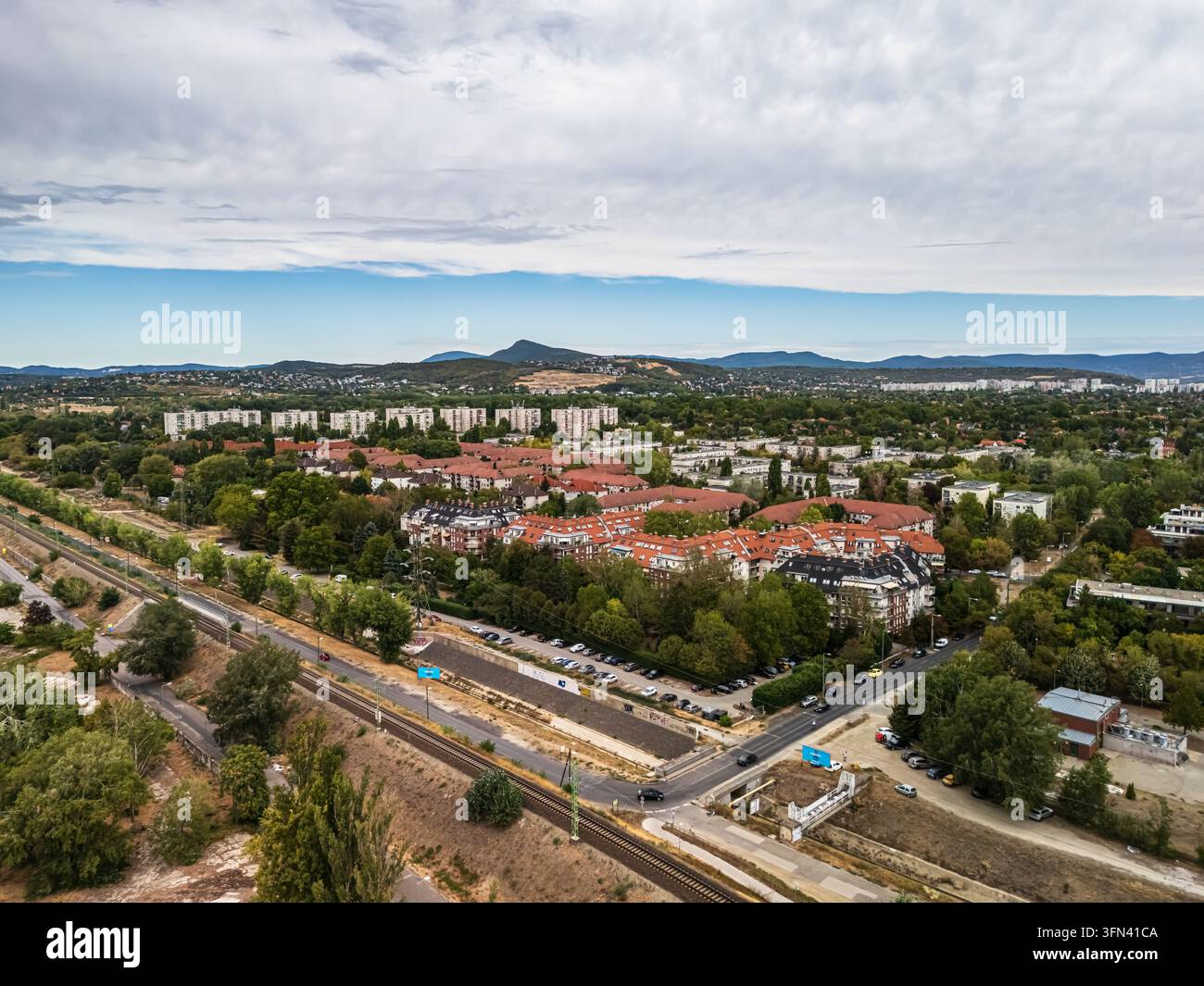Vista aerea dei quartieri residenziali, dei blocchi di appartamenti e delle infrastrutture ferroviarie a Óbuda, Budapest, Ungheria, con le colline di Buda e il monte Pilis Foto Stock